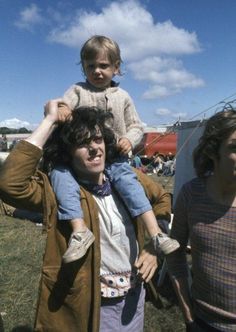 a woman carrying a child on her shoulders while standing next to two other women in a field