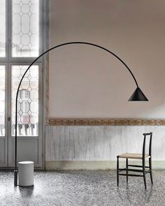 a chair sitting in front of a large window next to a tall black floor lamp