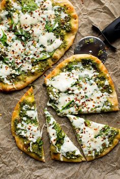 two pizzas with cheese and broccoli are on the table next to a spatula