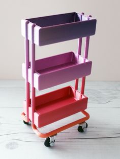 a pink and purple cart sitting on top of a wooden table next to a white wall