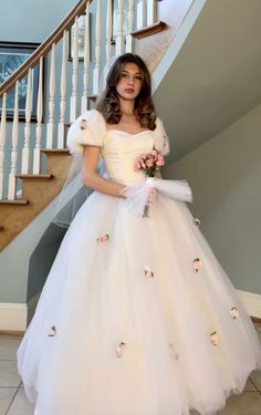 a woman in a white dress standing next to a stair case with flowers on it