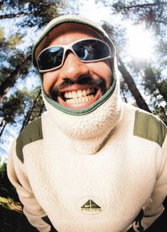 a man wearing sunglasses and a white jacket in the woods with his head covered by a scarf