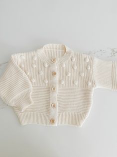 a white knitted sweater with buttons on the front and back, sitting on a marble surface