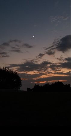 the sun is setting behind some trees and clouds in the sky, with one half moon visible