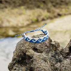 a blue and white bracelet sitting on top of a rock next to a body of water