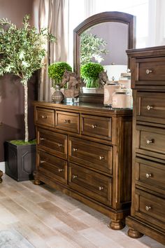 a bedroom with a dresser, mirror and potted tree