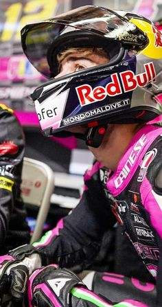 a man sitting on top of a motorcycle wearing a pink and black helmet with the word red bull written on it