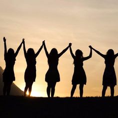 four women standing in the sunset with their arms up and one woman raising her hands