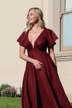 a woman in a red dress standing on the grass with her hand on her hip