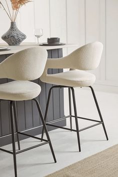 two white stools sitting next to each other in front of a counter with a vase on it