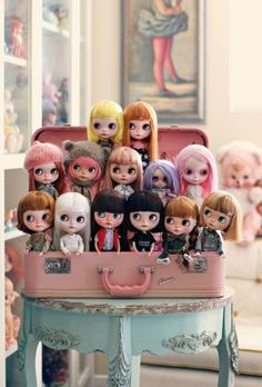 there are many dolls sitting in a suitcase on the table with other doll's