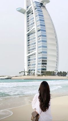 a woman walking on the beach in front of a tall building with a curved roof