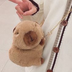 a person holding a brown teddy bear in their hand and wearing a white shirt with buttons on it