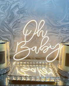 a neon sign that says oh baby next to two candles on a glass shelf in front of a marbled wall