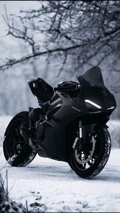 a black motorcycle parked on the side of a snow covered road in front of a tree