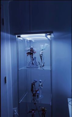 several action figures are displayed in a glass case with blue lighting on the wall behind them