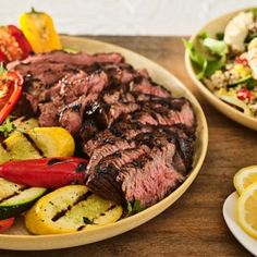 grilled steak and vegetables on a plate with lemon wedges next to the salad