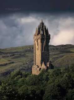 a tall tower sitting on the side of a lush green hillside under a cloudy sky