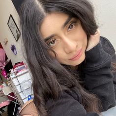 a woman with long black hair sitting in front of a mirror and looking at the camera