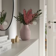 two vases with pink flowers on a white shelf next to a mirror and books