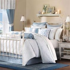 a bed with blue and white comforters in a bedroom next to a window on a rug