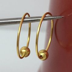 a pair of gold hoop earrings hanging from a hook on a metal bar with a red door in the background