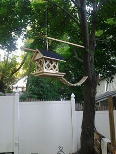 a bird house hanging from the side of a tree next to a white picket fence