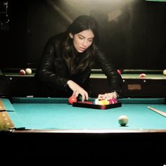 a woman is playing pool in a dark room with balls on the table and cuesticks