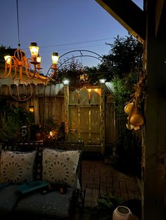 an outdoor seating area is lit up at night with lights on the fence and hanging lanterns