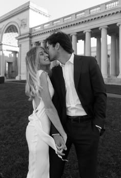 a man and woman kissing each other in front of a building with columns on it