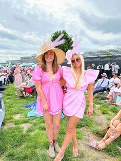 two women in pink dresses and hats standing next to each other at an outdoor event