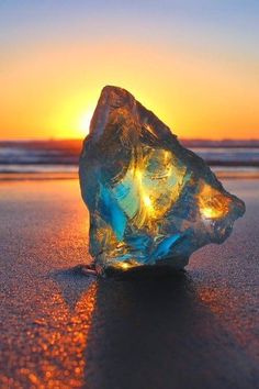 an ice cube sitting on top of a beach next to the ocean at sunset or dawn