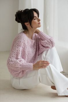 a woman is sitting on the floor wearing a pink sweater and white pants