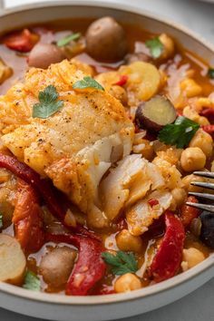 a white bowl filled with chicken, beans and vegetables next to a fork on top of a table