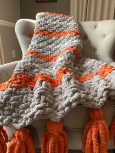 an orange and gray crocheted blanket sitting on top of a white chair