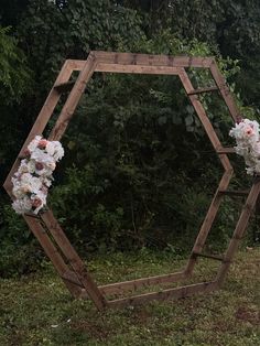 a wooden hexagonal mirror with flowers on it in front of some bushes and trees