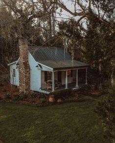 a small blue house sitting in the middle of a yard next to trees and bushes