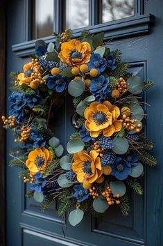 a wreath with yellow and blue flowers hanging on the front door's green door