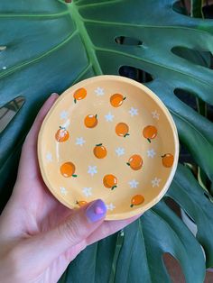 a hand holding a yellow bowl with oranges on it and white stars around the rim