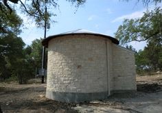 an old round brick structure in the middle of a dirt field with trees around it