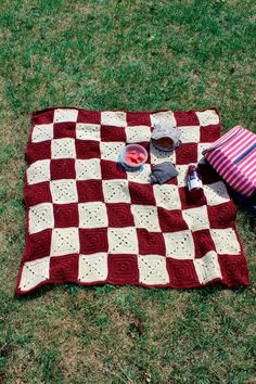 a red and white blanket sitting on top of a grass covered field next to a bag