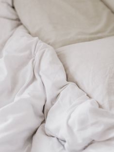 an unmade bed with white sheets and pillows