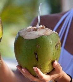 a woman holding a green coconut with a straw in her hand