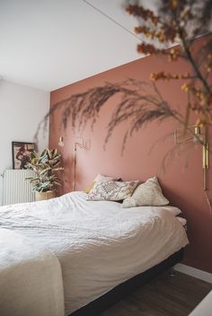 a bedroom with pink walls, white bedding and plants on the wall behind it