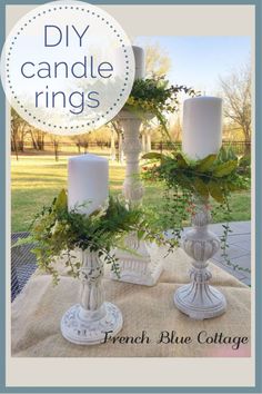 two white candles sitting on top of a table covered in greenery and ivys