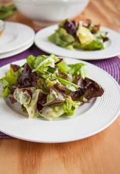 two white plates filled with salad on top of a wooden table