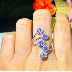 a woman's hand with three rings on it and flowers in the back ground