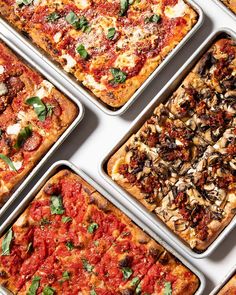 six different types of pizzas in pans on a white counter top with basil and mushrooms