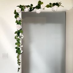 a white frame with flowers and greenery on the wall in front of a mirror