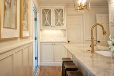 a white kitchen with marble counter tops and gold accents on the cabinet doors, along with two stools